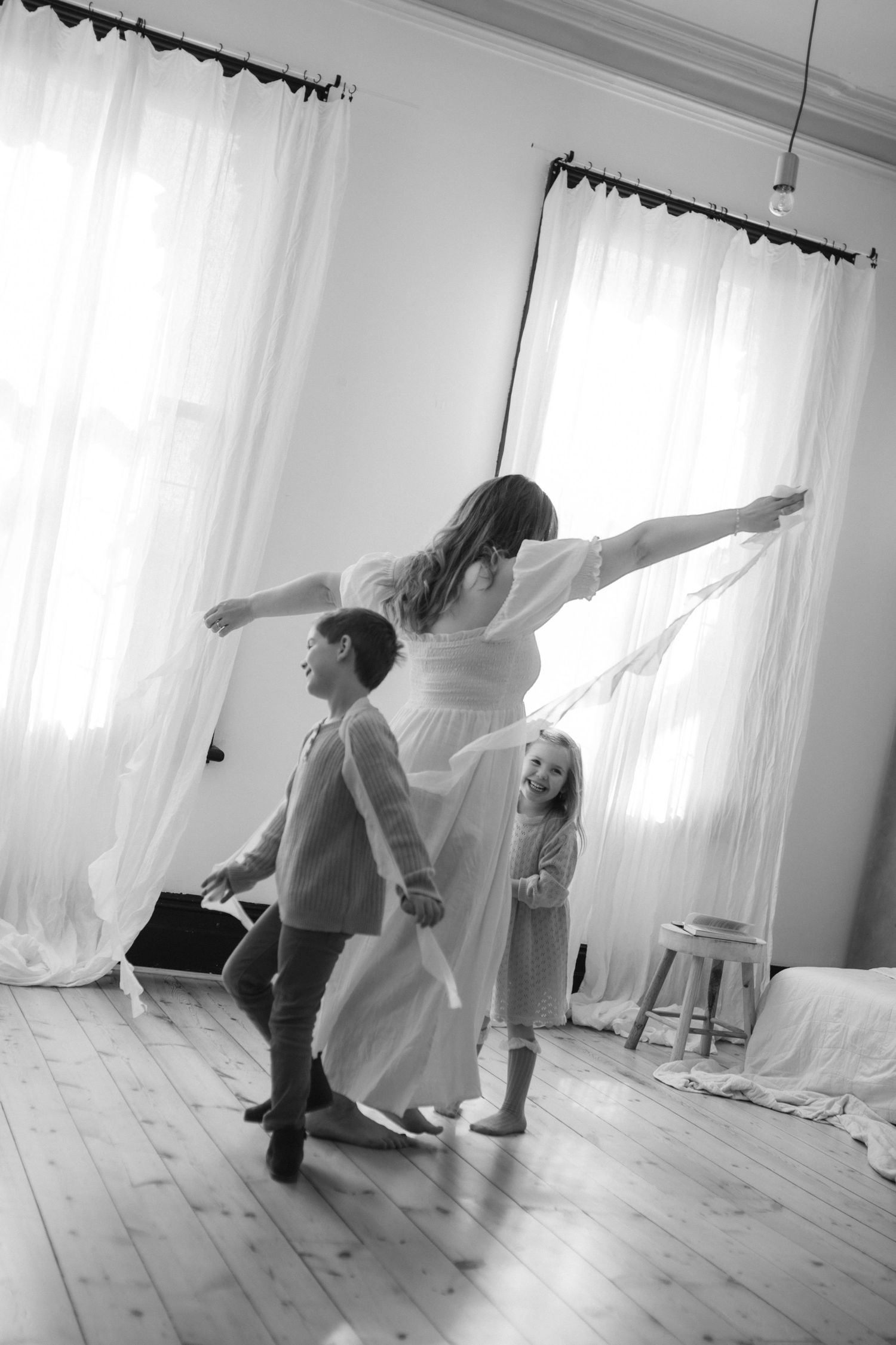 Black and white photo of people dancing together in a bright room with white curtains and wooden floors.