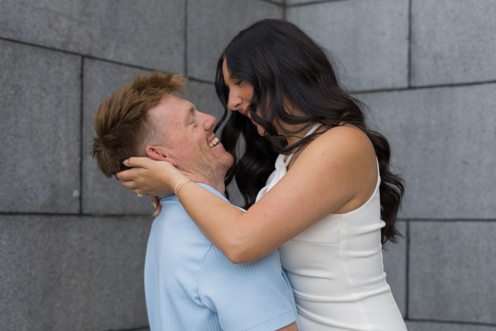 A romantic couple sharing an intimate moment against a grey concrete wall background.