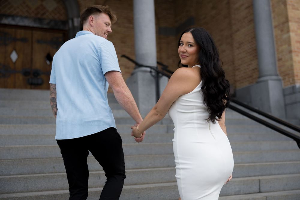 A couple in coordinating white and blue outfits pose together on stone steps.