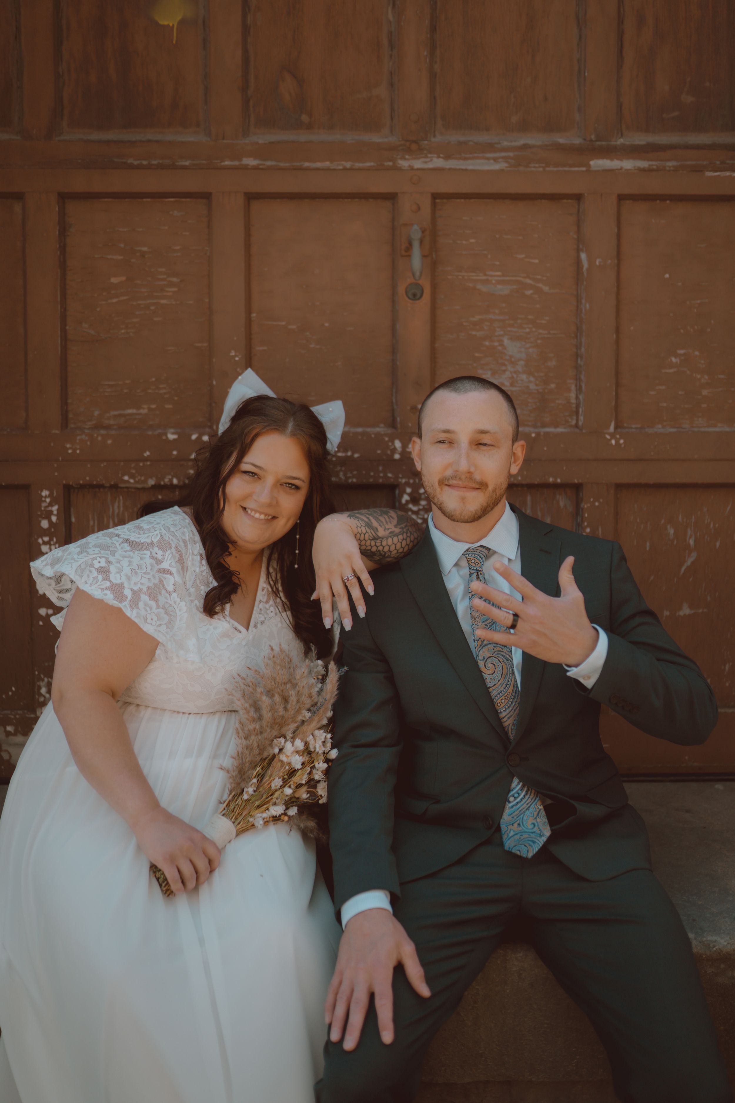 Newlyweds share playful moments against a rustic wooden backdrop during their wedding photoshoot.