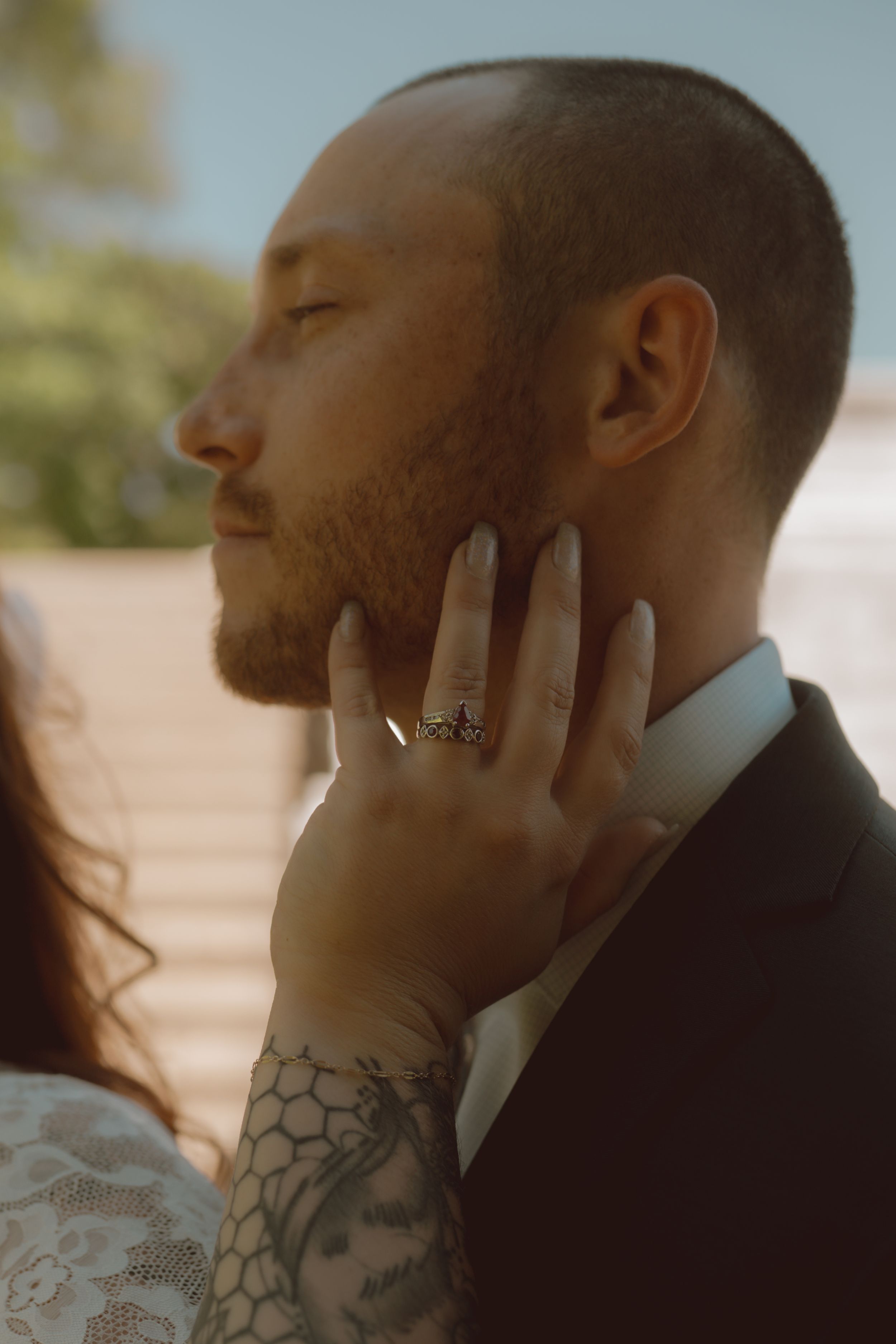 Close-up detail shot of a tattooed groom's profile with soft, natural lighting.