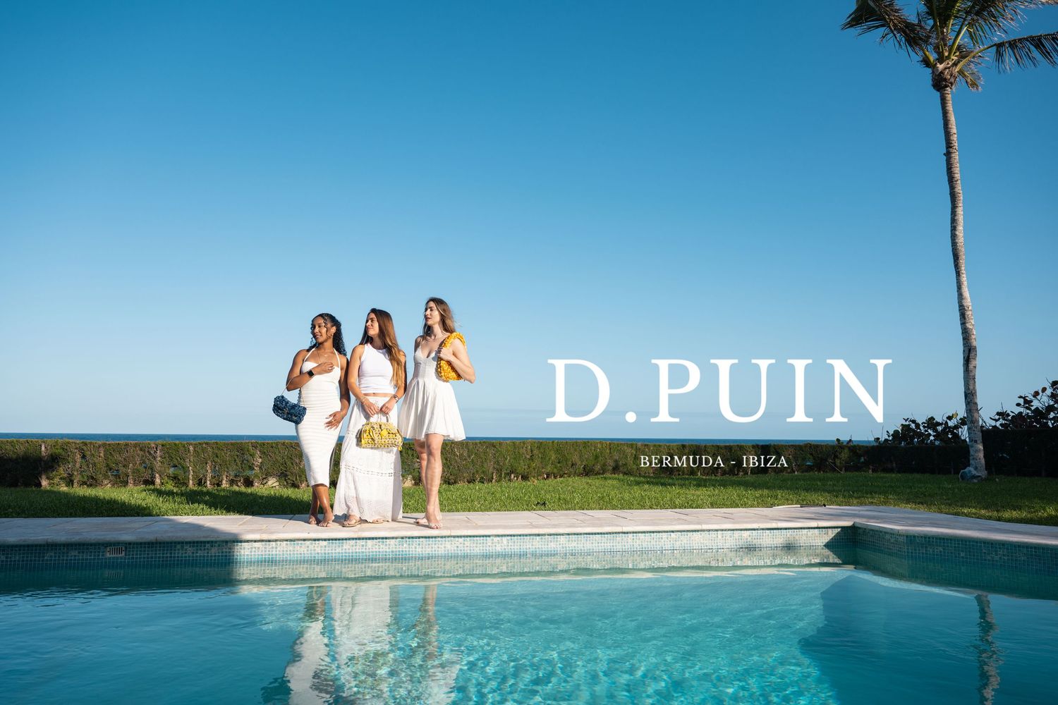 Three friends in white summer dresses pose by a swimming pool with ocean view and palm tree in Hawaii.