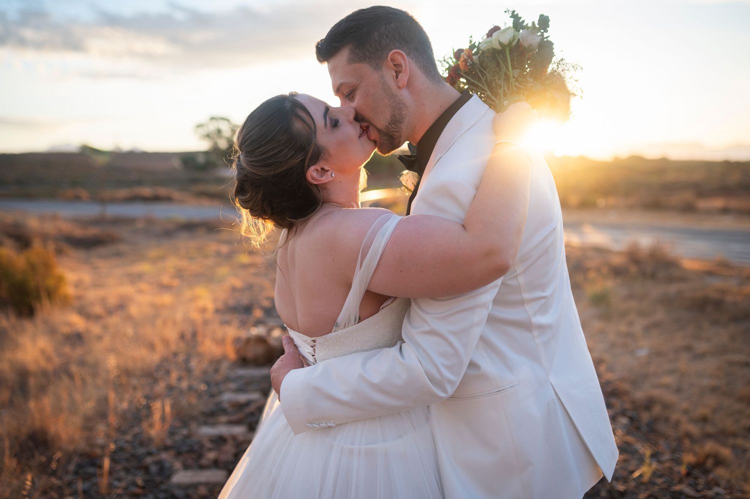 Sunset wedding portrait with couple embracing in desert landscape.