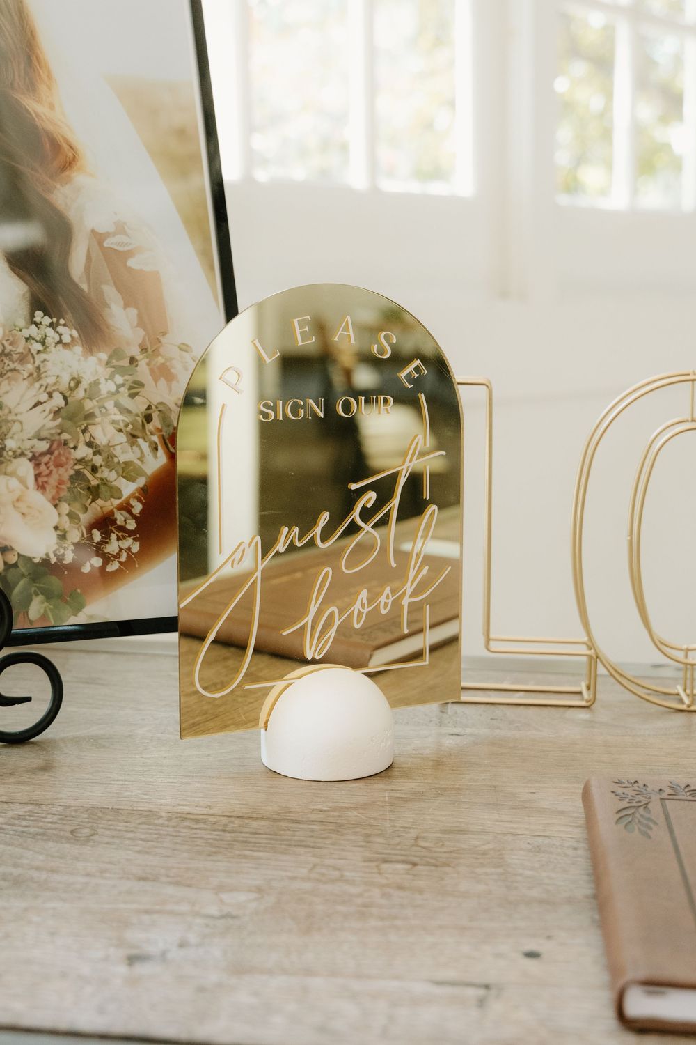 Gold mirror guest book sign display on wooden table with modern wedding decor elements.