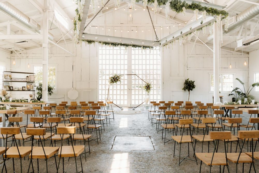 Modern white wedding venue with rows of wooden chairs and natural light streaming through windows.