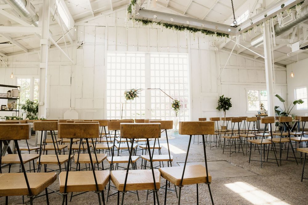 Modern industrial wedding venue with wooden chairs and white walls filled with natural light.