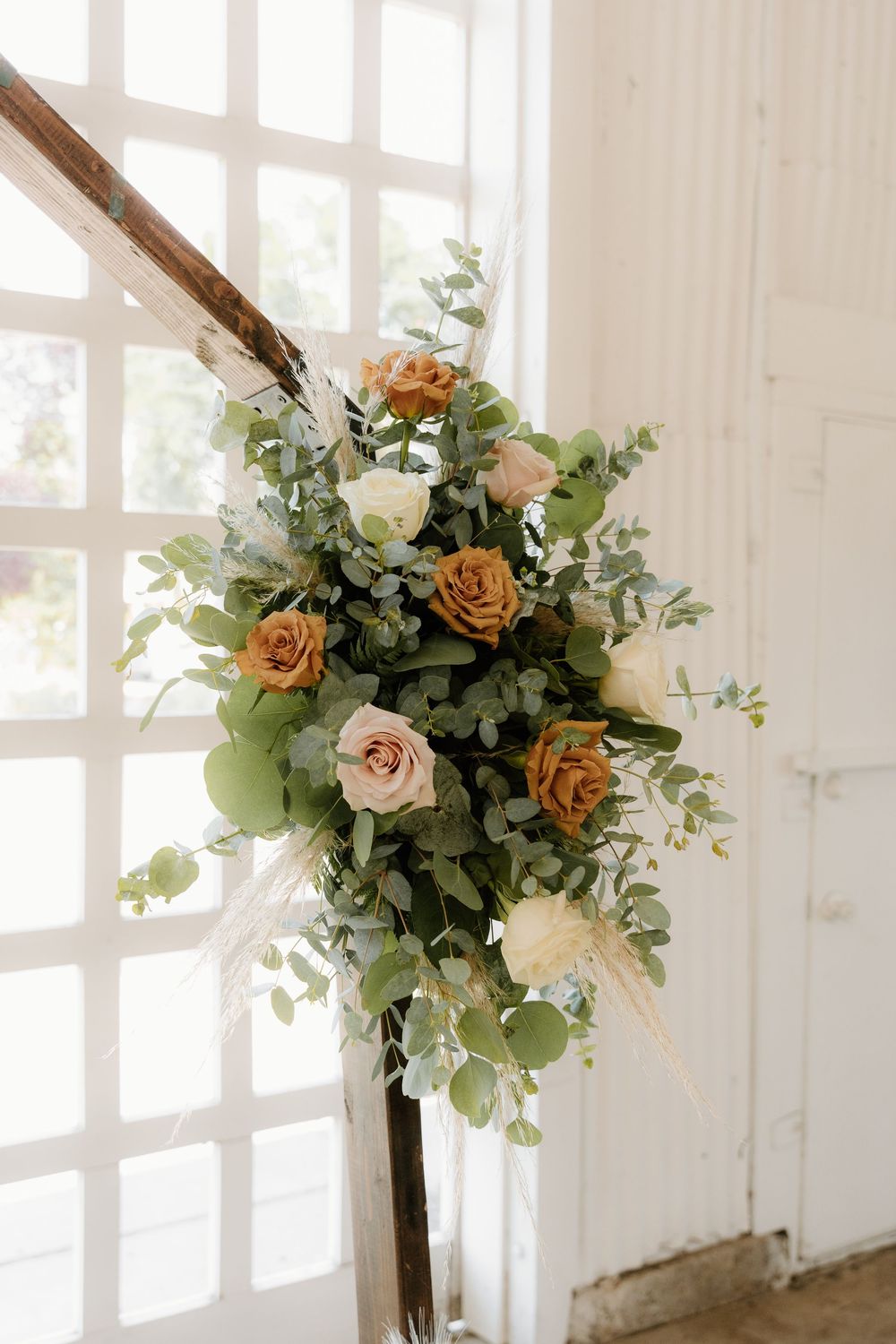 Elegant floral arrangement with peach and cream roses mixed with eucalyptus leaves against a bright window backdrop.