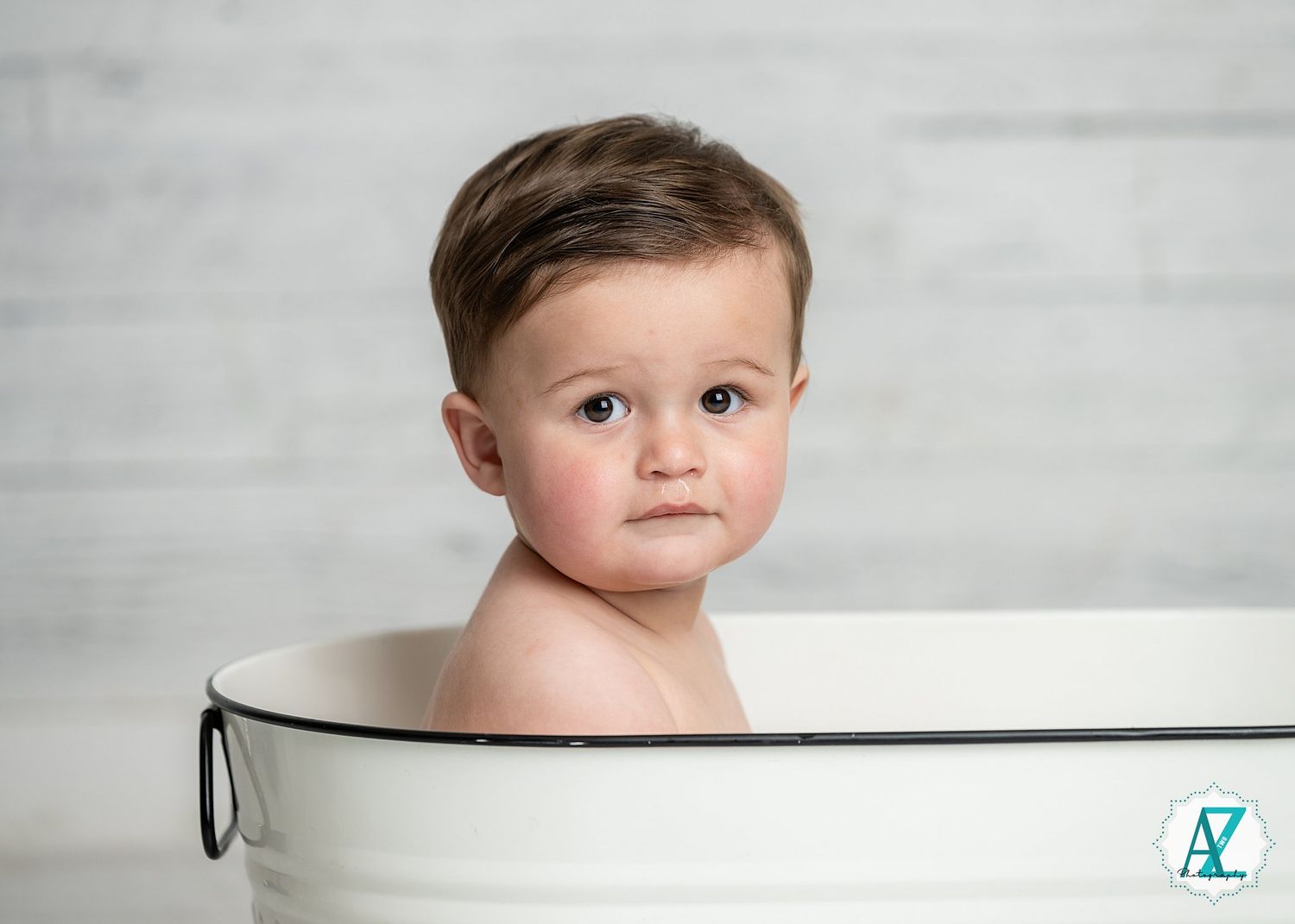 Portrait of a young child sitting in a white bathtub against a light gray background.