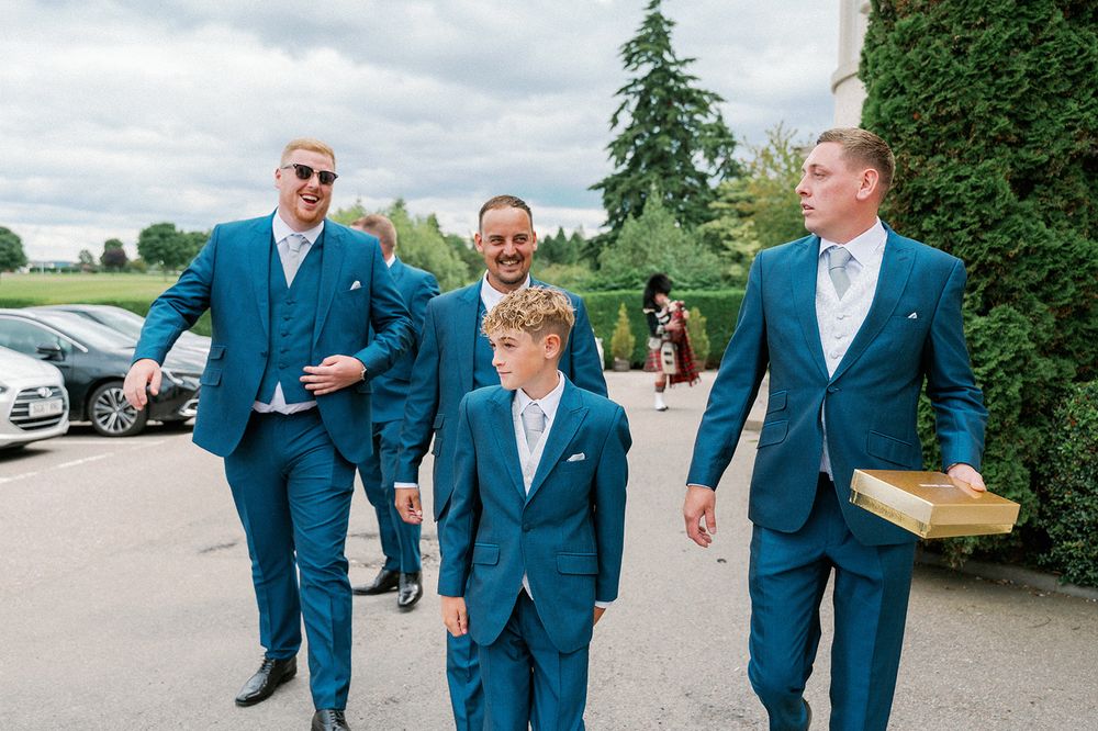 Groomsmen in navy blue suits walk and laugh together outdoors.