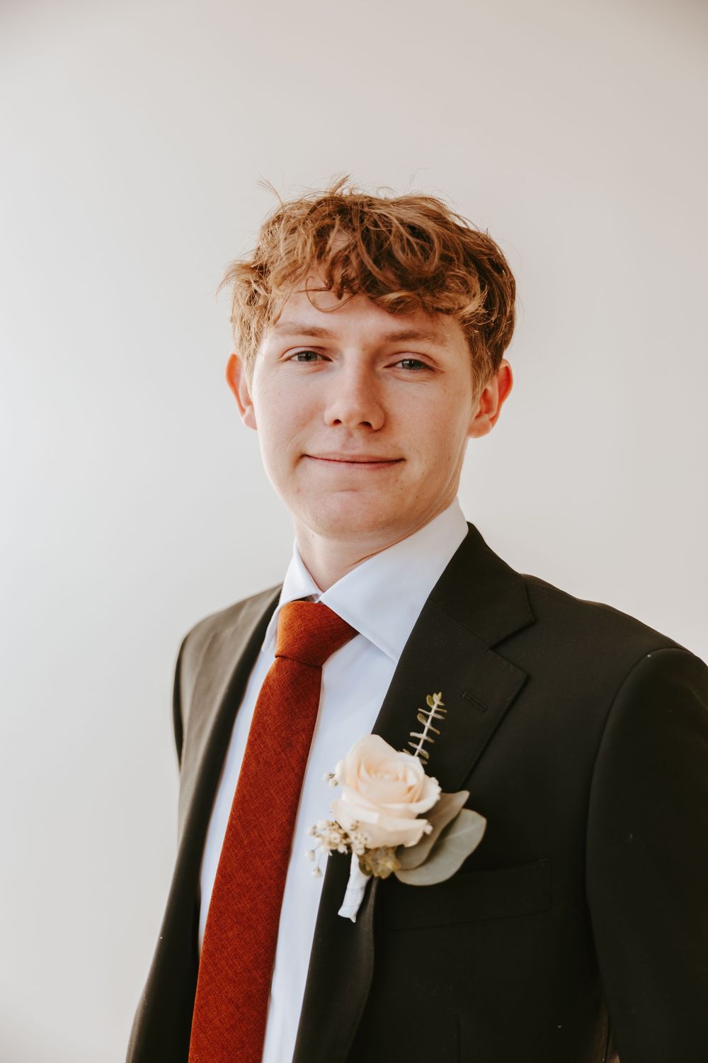 Formal portrait in dark suit with red tie and white boutonniere against light background.
