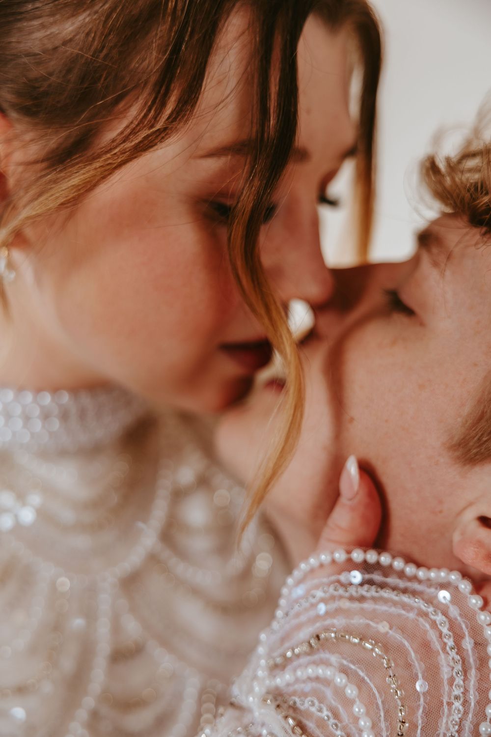 A romantic couple sharing an intimate moment, with the bride wearing a delicate beaded gown with pearls.