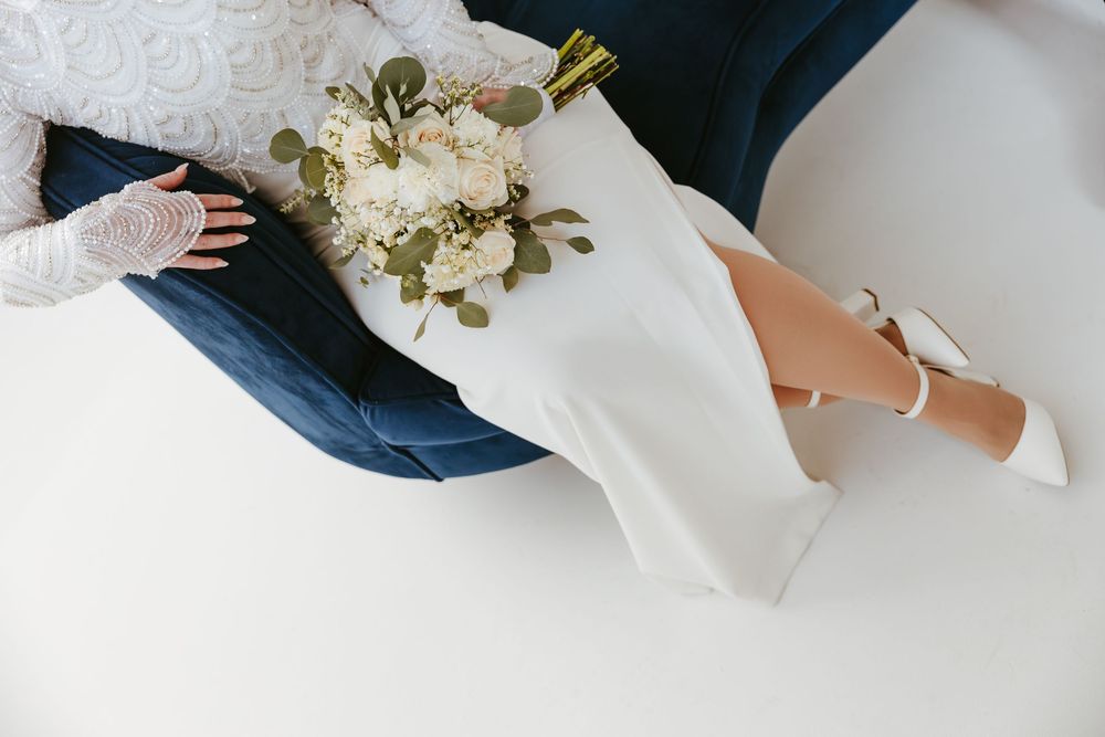 A white wedding dress with floral details and blue denim contrasts against a stark white background.