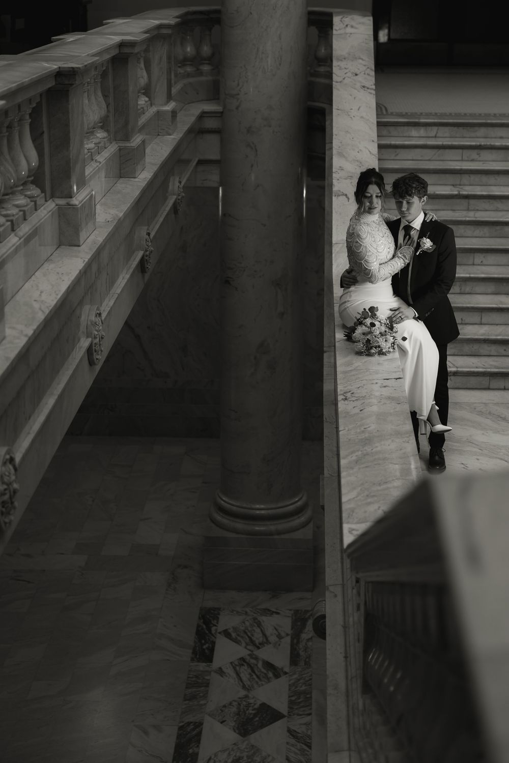 Black and white artistic photo of newlyweds posed by classical stone columns in architectural setting.