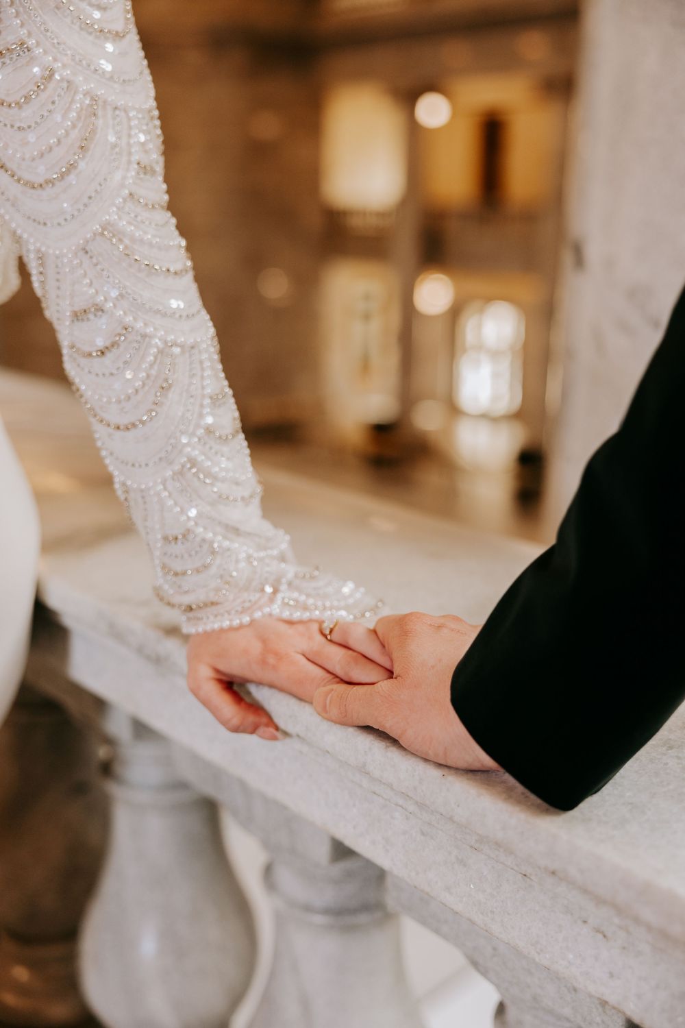 Close up of hands touching gently over white lace detail of a wedding dress in an elegant interior setting.