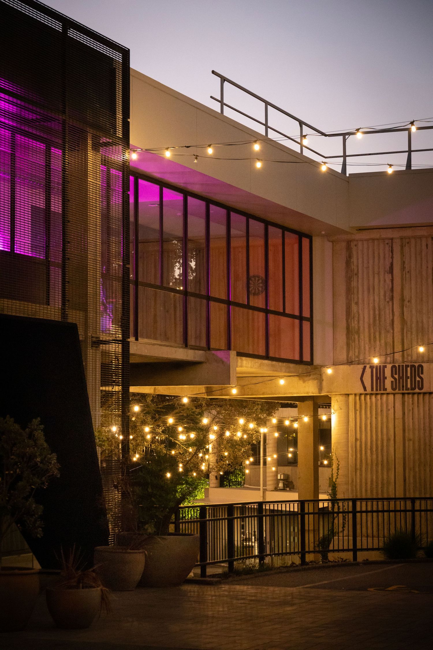 Exterior of a two-story hospitality venue with festoon lighting and pink uplighting at dusk.