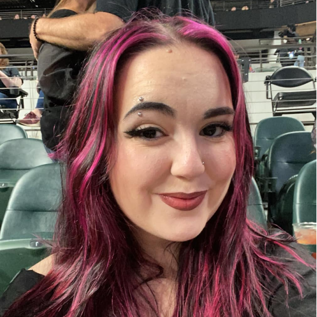 Selfie showing vibrant pink and purple dyed hair at a stadium with stadium seats visible in background.