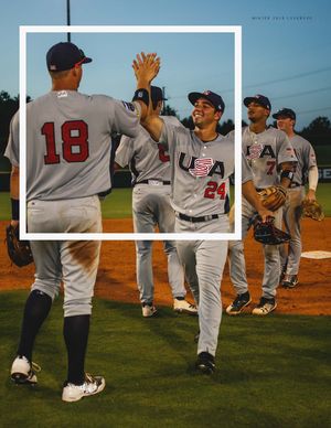 Two USA Baseball Collegiate National Team players in jerseys 18 and 24 celebrating with high fives on field.