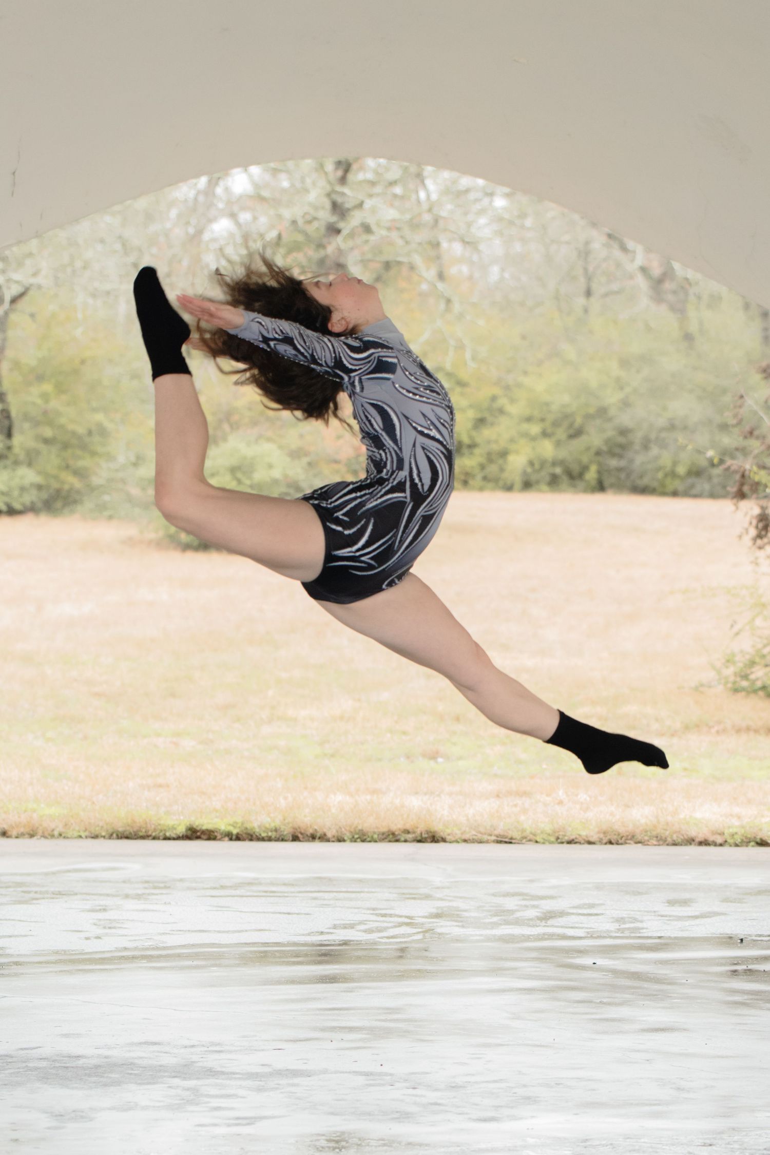 A dancer in black leaps gracefully through the air, demonstrating impressive flexibility and form above a reflective surface.