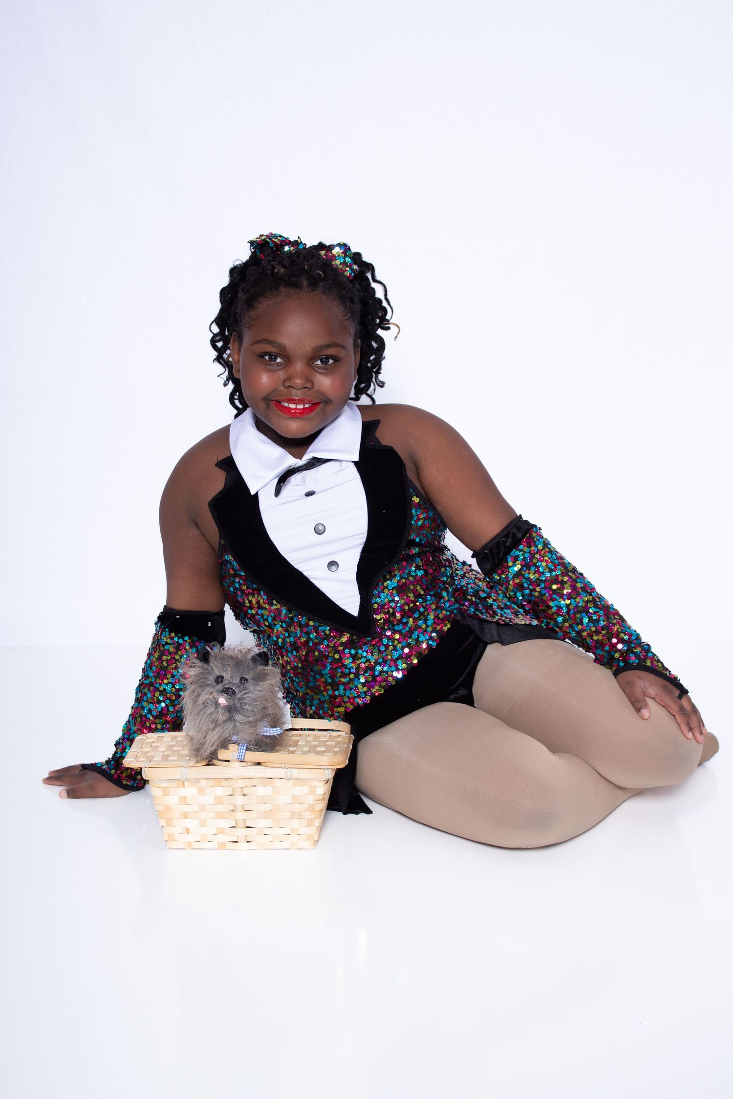 A dancer in a sparkly black leotard and tights poses gracefully with a plush gray bunny on a white backdrop.