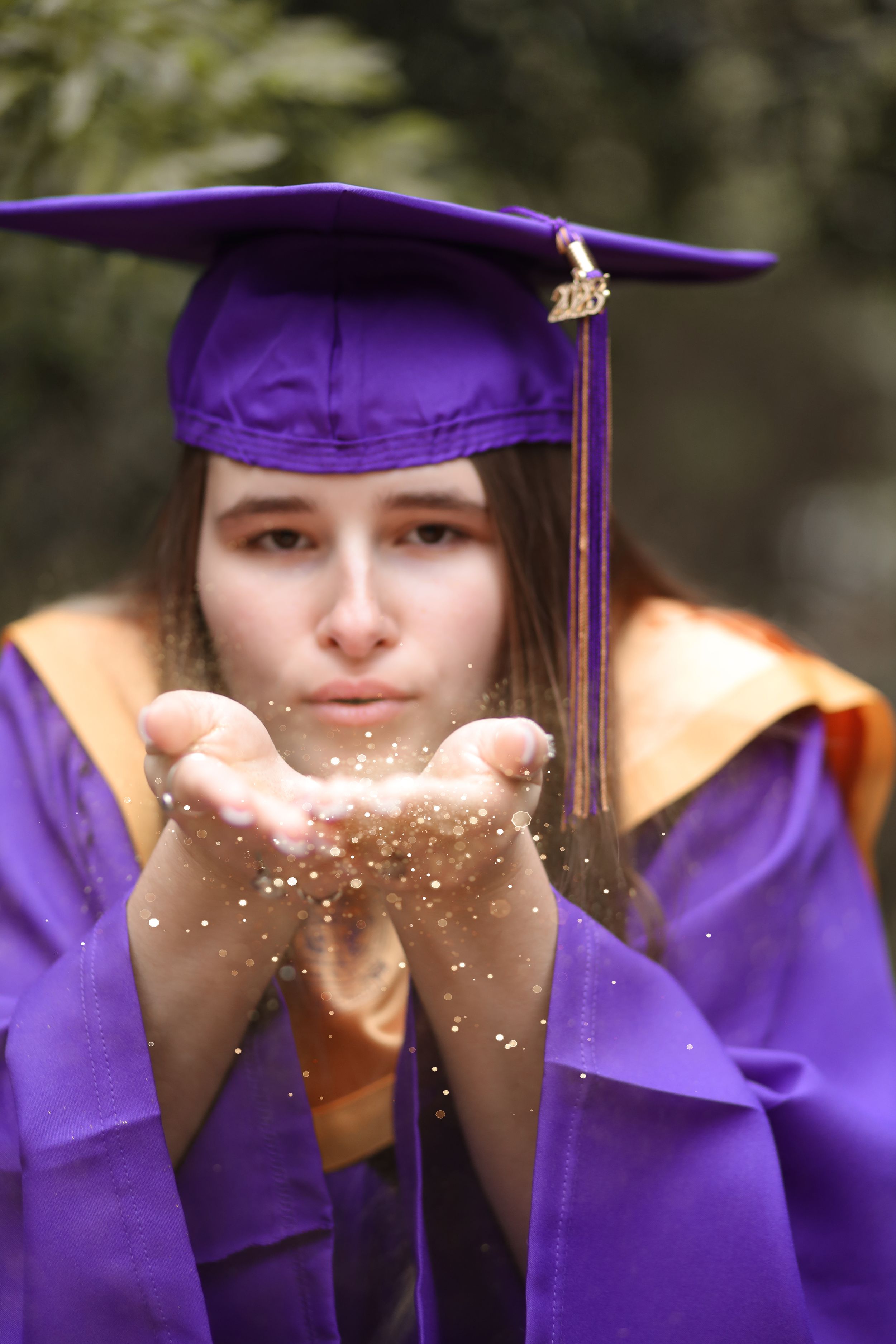 A graduate in purple cap blowing glitter from their hands in a playful celebration moment.