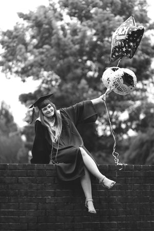 A graduate in cap and gown sits atop a brick wall in a creative photo sequence showing playful climbing movements.