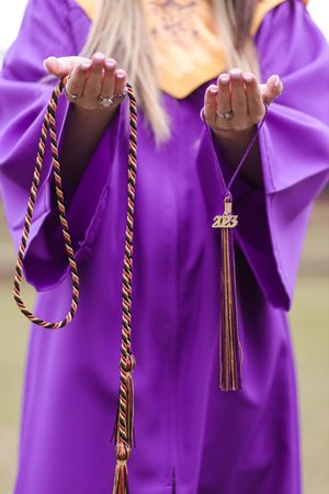 Graduation ceremony showing students in purple robes holding tasseled honor cords against a blurred background.