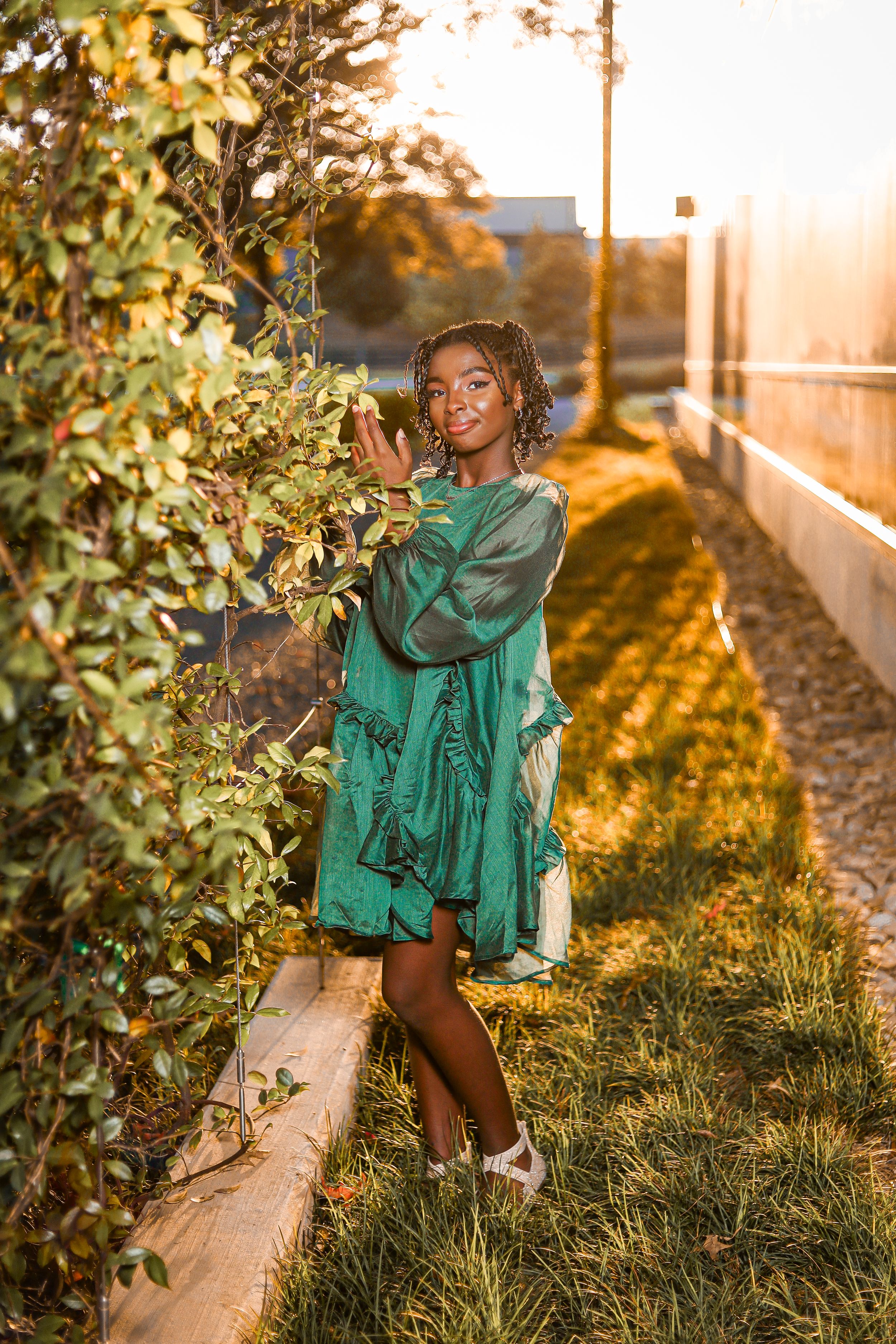 A sunlit autumn portrait featuring someone in a flowing emerald green dress standing beside lush foliage at golden hour.