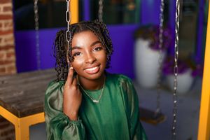 Person wearing green top relaxes on a porch swing with a gentle gaze and braided hairstyle.