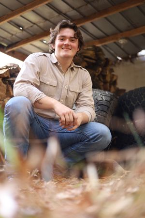 A person in a beige shirt and jeans sits on a bench in a rustic indoor setting.
