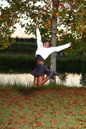An energetic mid-air jump captured against a backdrop of fall trees with scattered red leaves on the ground.