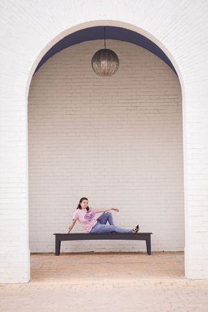 Person relaxing on bench under white archway with pendant light in minimalist architectural setting.