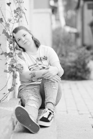 A person in casual attire sitting on a step with sneakers and jeans, shown in black and white photography.