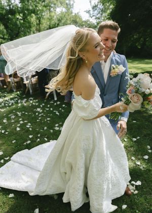A joyful wedding moment captured with flowing veil and white dress against green garden backdrop.