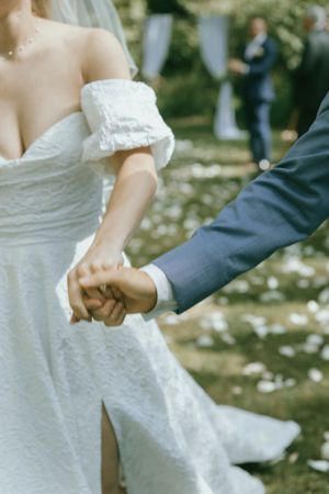 Close-up of joined hands during a wedding ceremony with flower petals scattered on the ground.