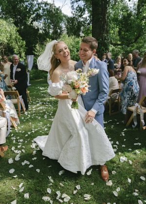 Happy couple celebrates during their garden wedding ceremony surrounded by rose petals and guests.