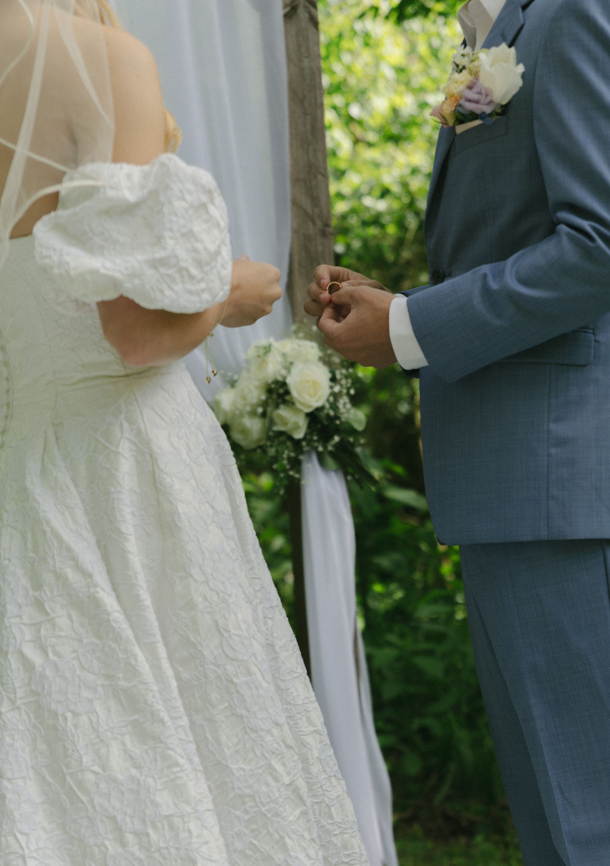 Close-up of bride and groom exchanging rings during outdoor garden ceremony.