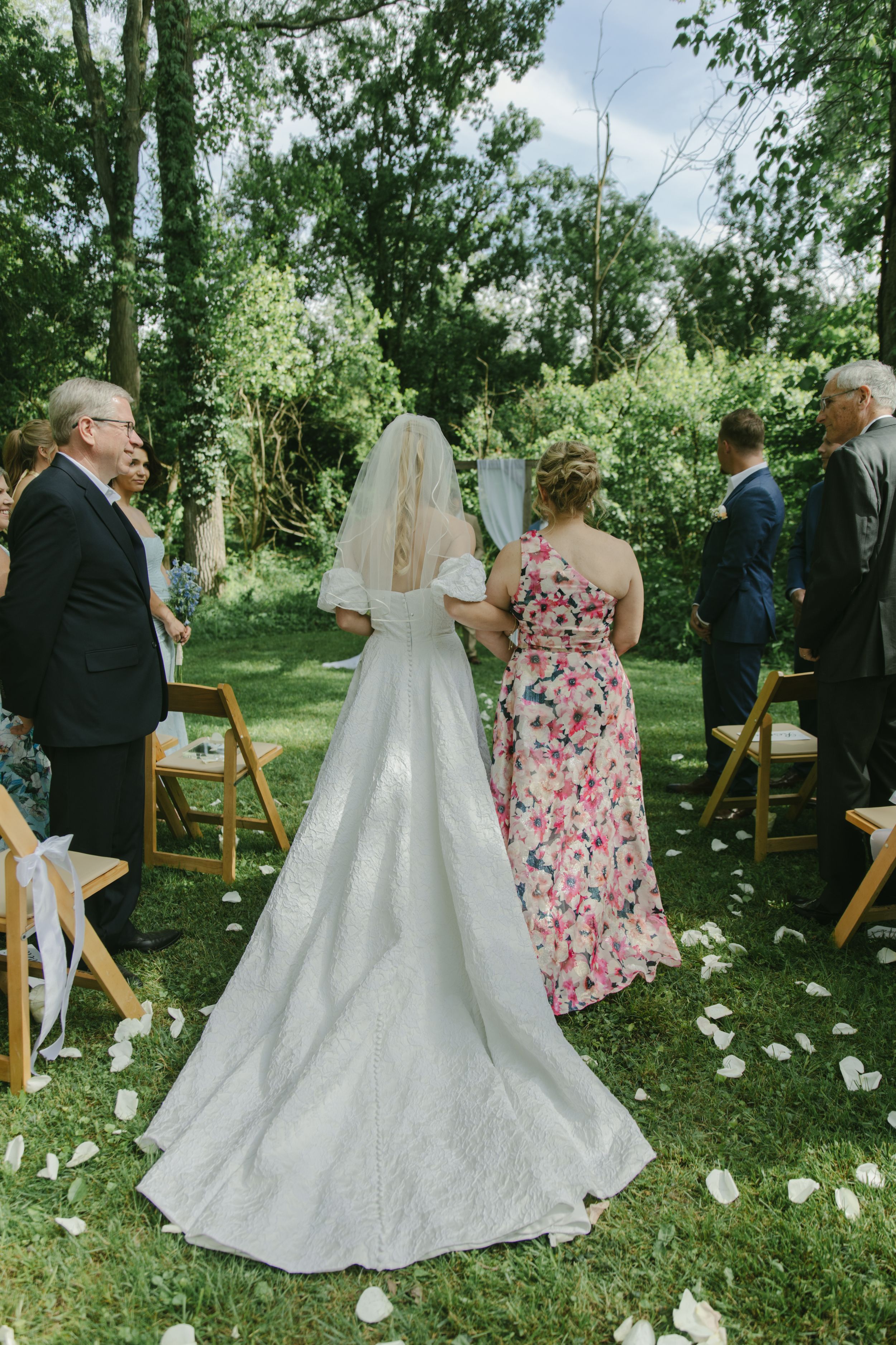 A wedding ceremony in a garden setting with white flower petals scattered on the grass.