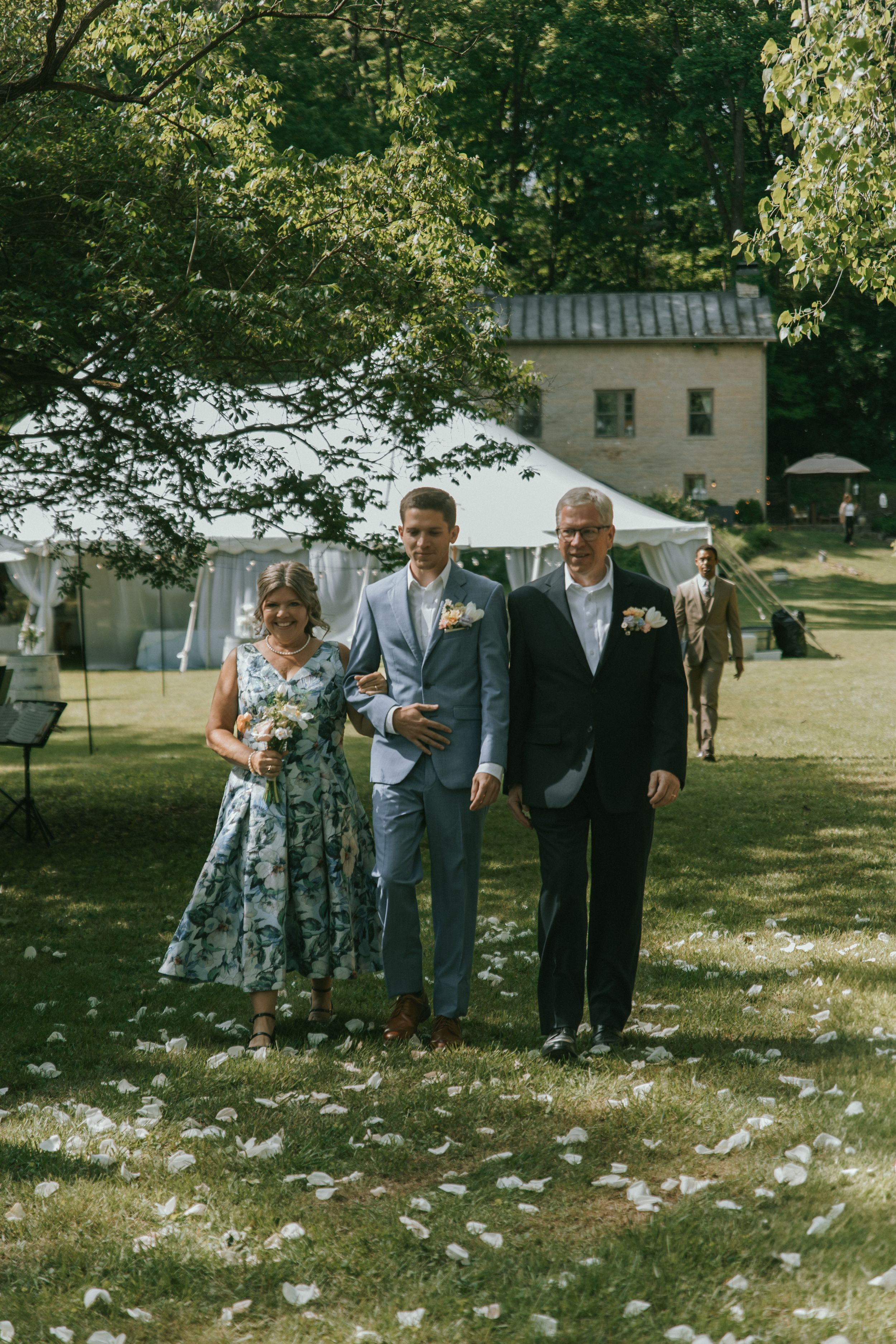 Wedding party members walking across a lawn with scattered petals and a building in the background.