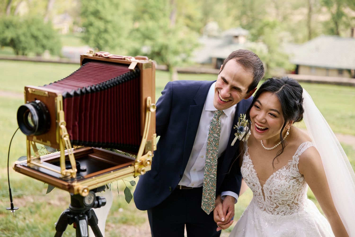 A couple taking photographs with a vintage wooden camera in a garden setting at their wedding celebration.