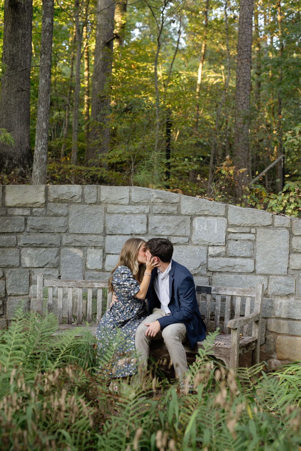 Stone wall bench surrounded by lush ferns and trees in a romantic garden setting.