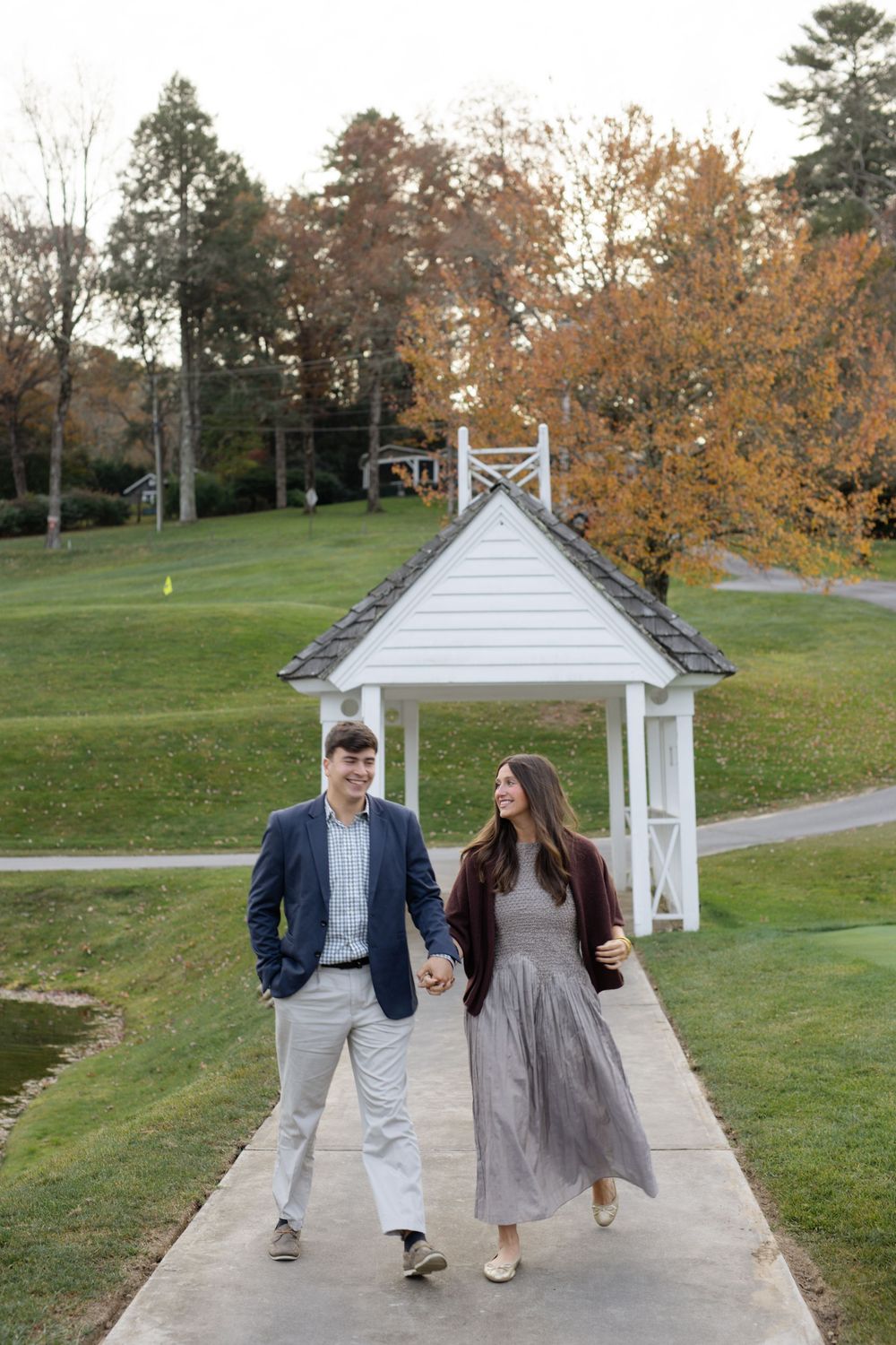 Couple walking along path near white gazebo during fall season.