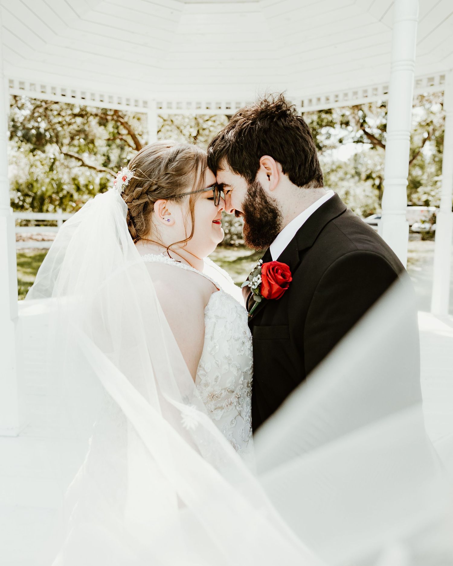 White veil flows dramatically during an intimate wedding moment under a gazebo.