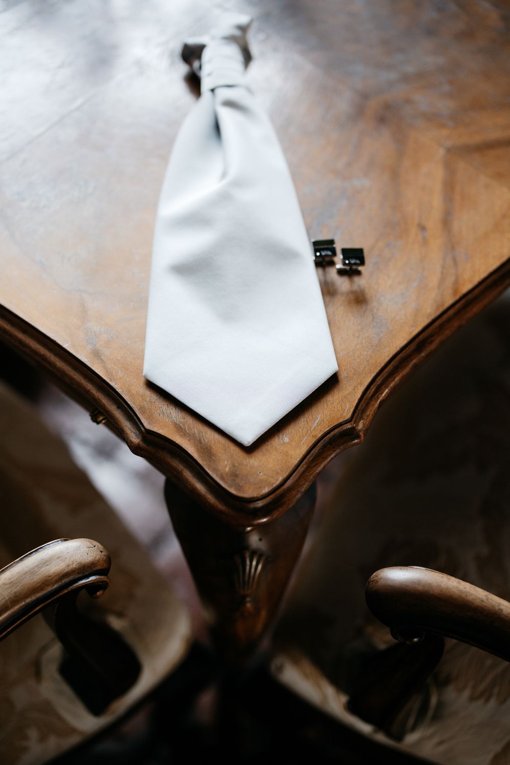 White necktie laying on ornate wooden furniture with blurred details in background.