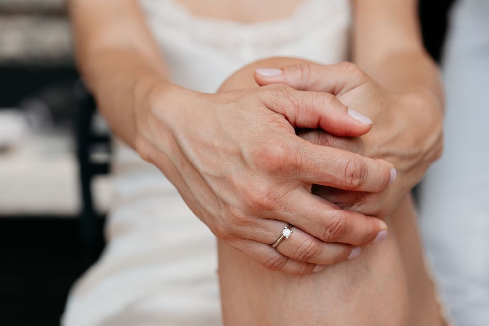 Close up of clasped hands showing a sparkling engagement ring on a finger in a white garment.