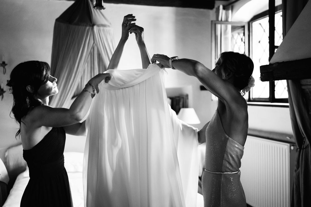 Silhouetted figures hold up a white wedding dress against a bright window.