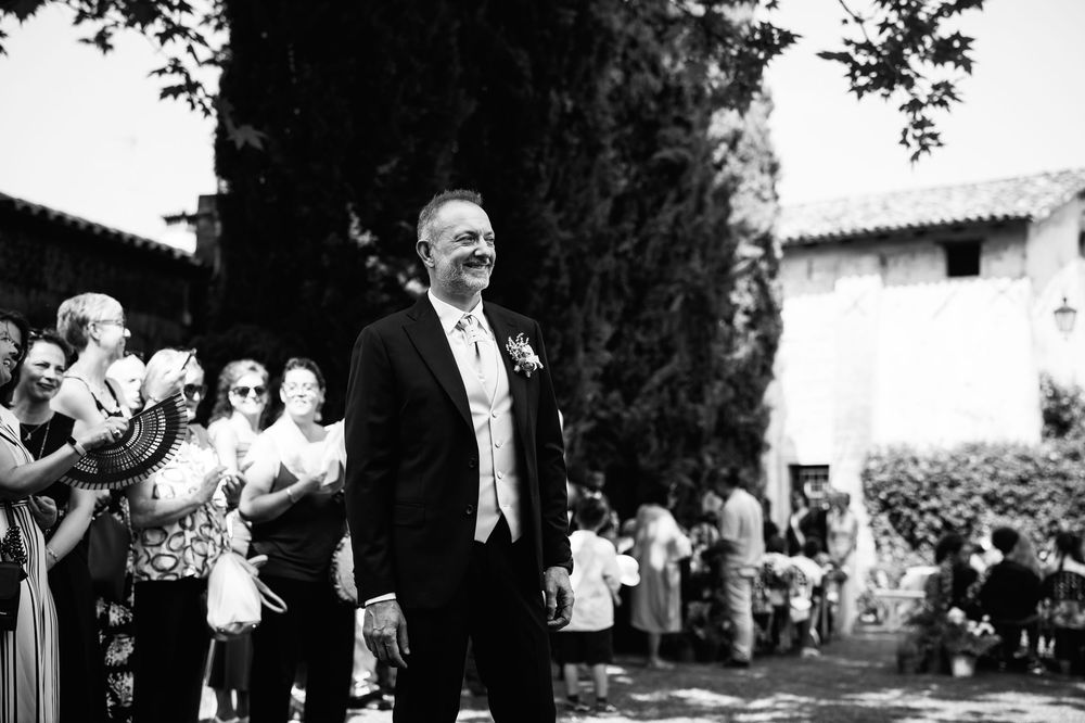 Wedding guests applauding during an outdoor ceremony with cypress trees and villa in the background.