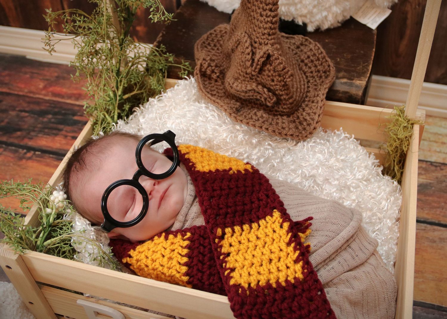 A newborn photography session featuring a knit wizard costume with round glasses and brown owl prop on white bedding.
