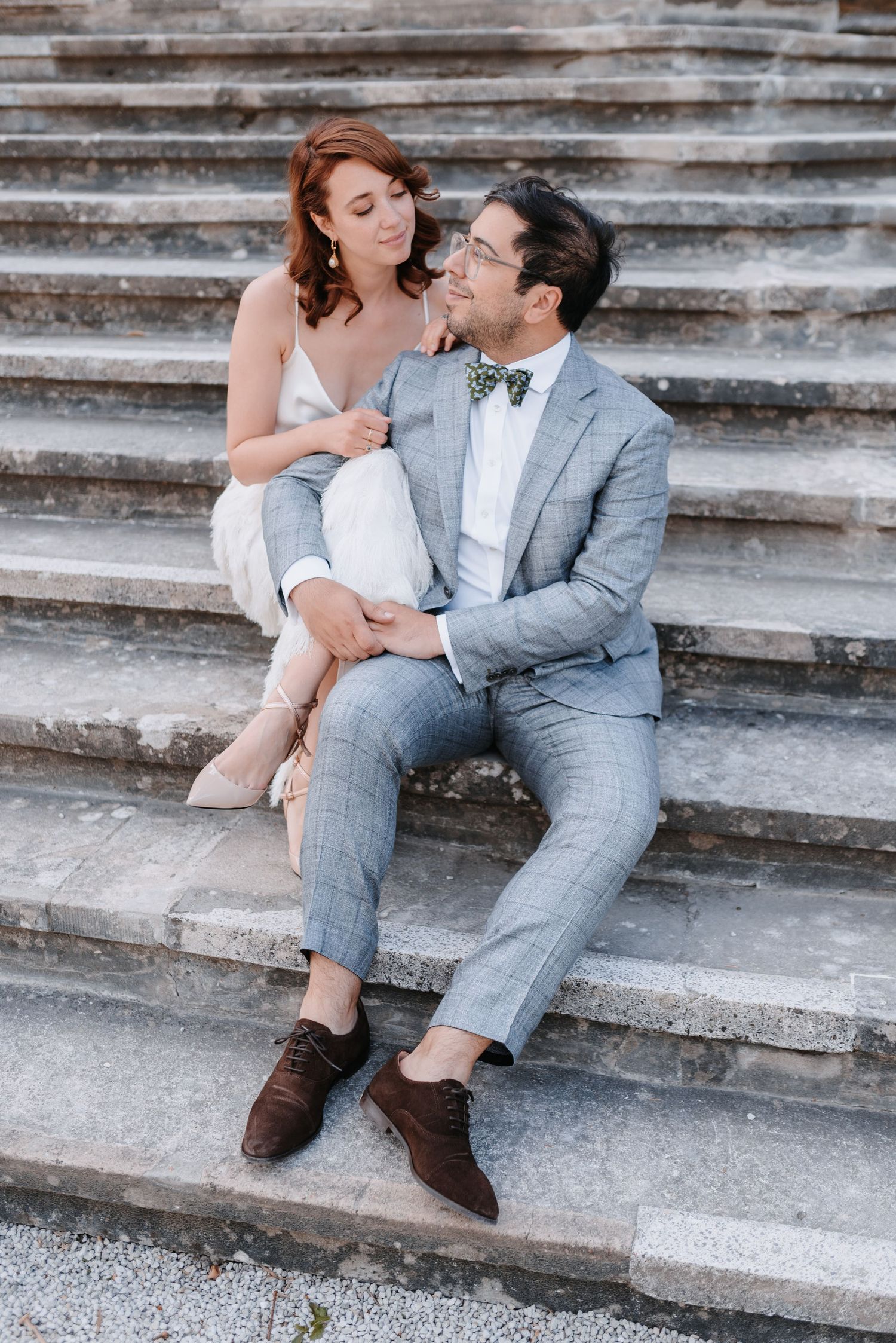 Stylish couple in formal attire sitting on stone steps during engagement photo session.