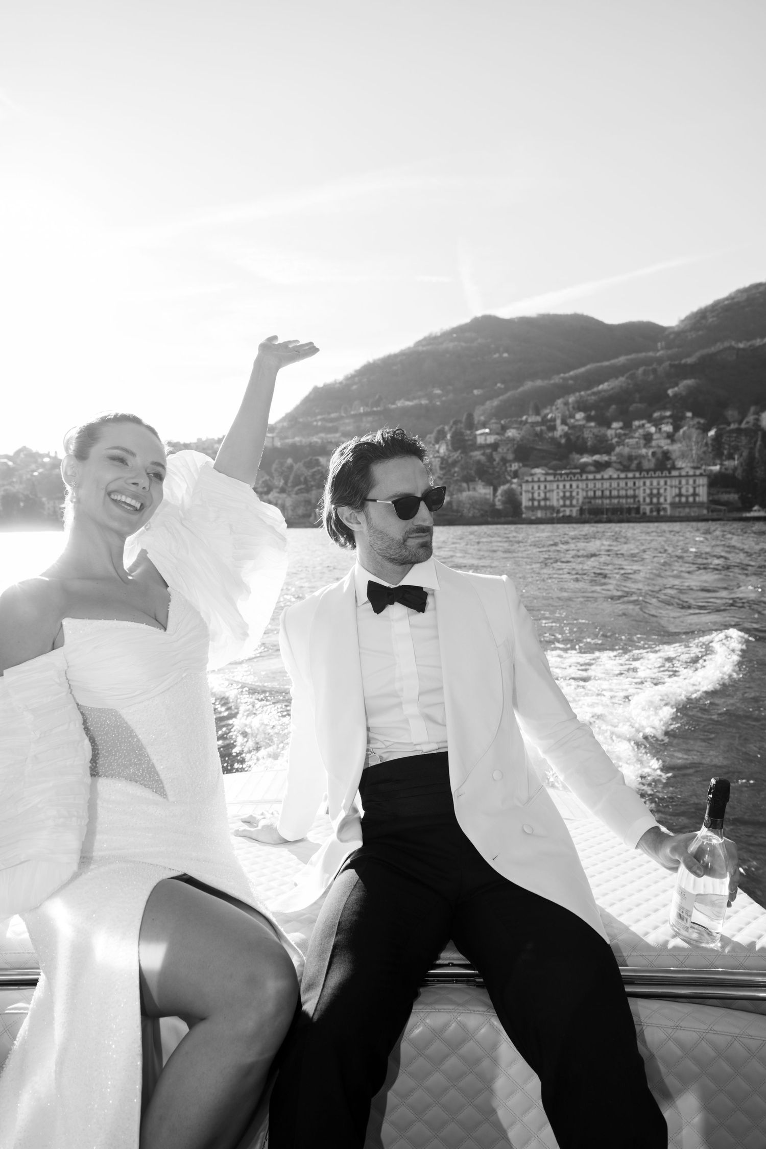 Elegant couple relaxes on boat deck with champagne during sunset cruise along scenic Mediterranean coastline.