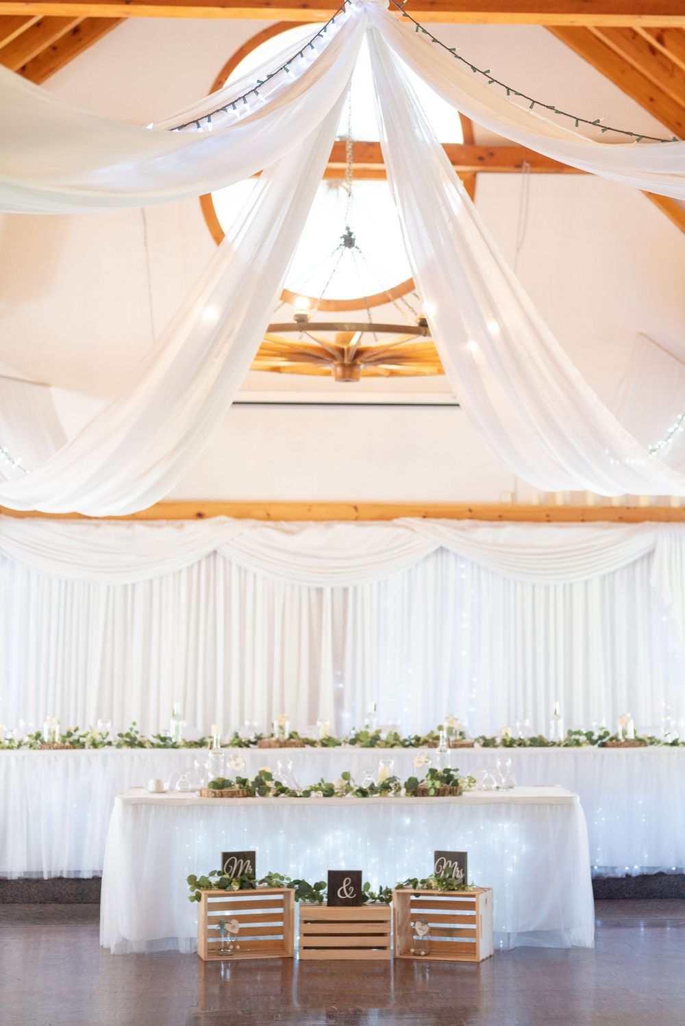 Elegant wedding reception setup with white draping and rustic wooden decor.